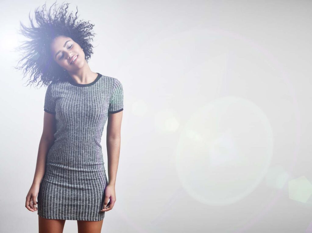 Smiling woman with curly hair feeling joyful and hopeful in bright light, symbolizing recovery and renewal.