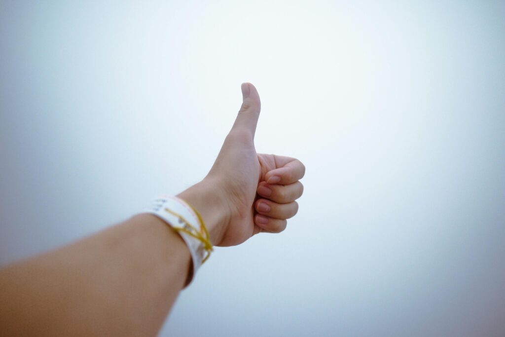 Person's hand giving a thumbs up with a medical wristband against a light background, signaling hope in recovery.