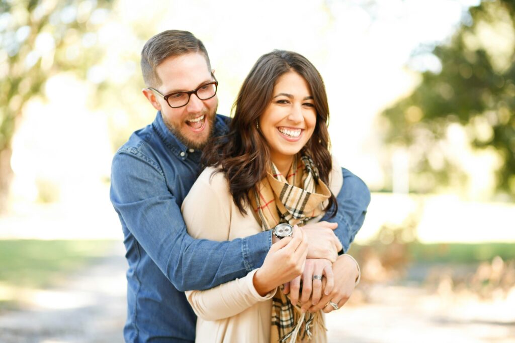 Smiling couple embracing outdoors, enjoying a happy moment together in a sunlit park.